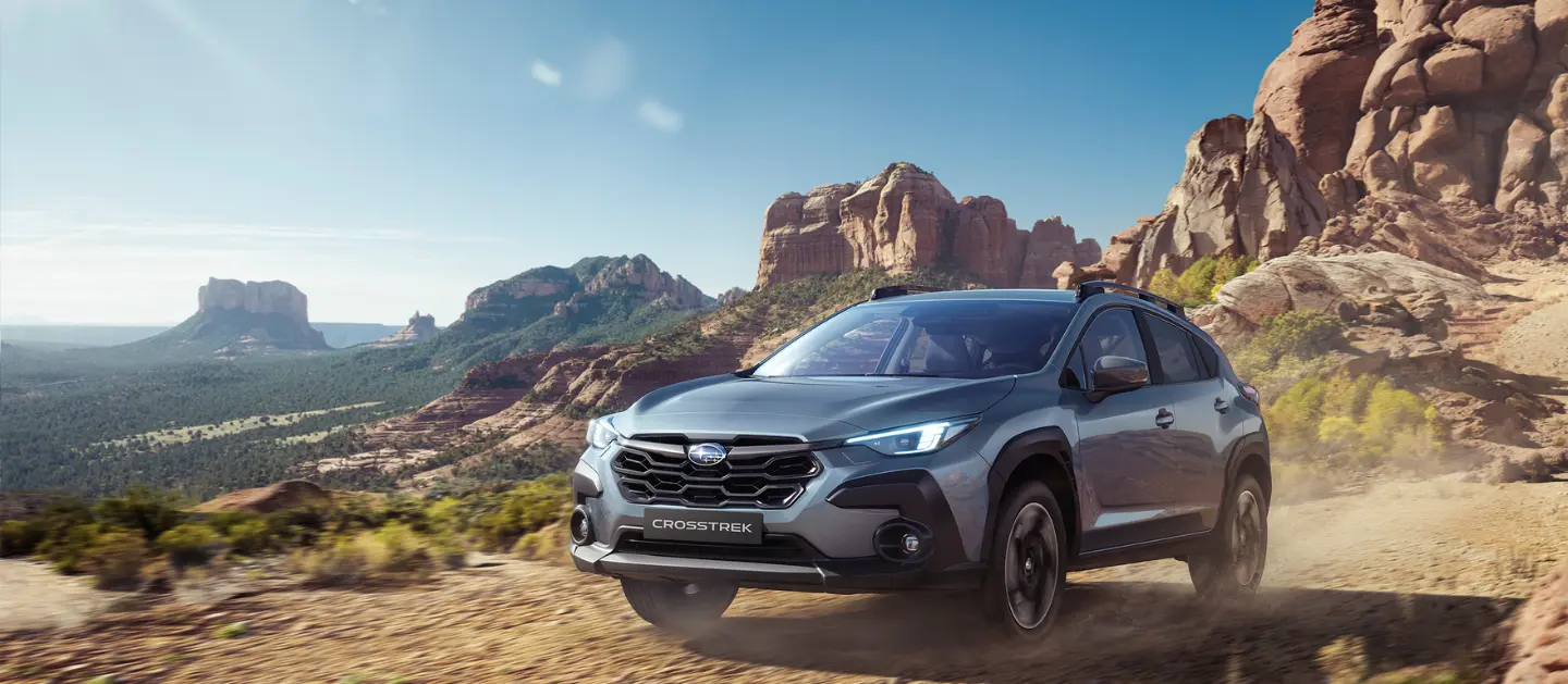 Subaru Crosstrek en terreno arenoso con cañones de fondo.